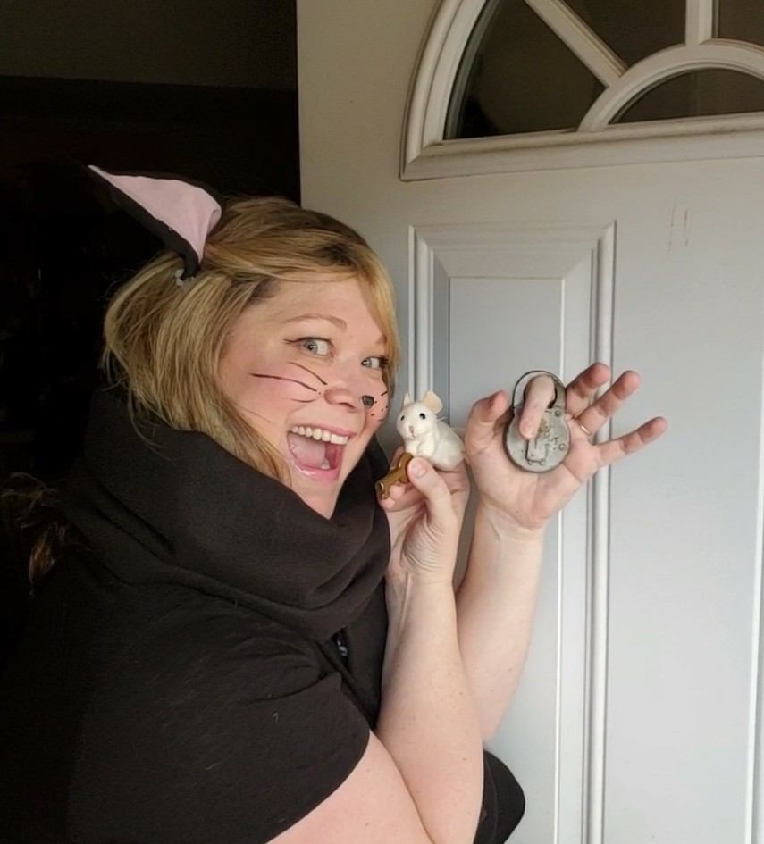 Marcia Blake laughing in cat makeup, pressing a toy mouse and a brass key to her cheek while holding up a padlock